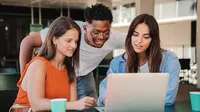 Three young adults gathered around a laptop looking at its screen